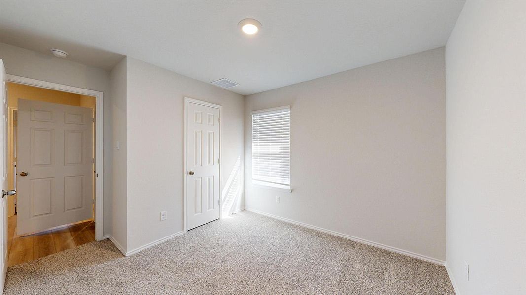 A well-lit bedroom features plush carpeting and a bright window with blinds.