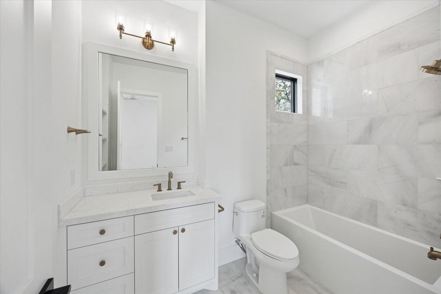 Well appointed ensuite bath featuring quartz countertops, a custom shaker vanity, and brushed brass fixtures for a timeless finish. Marble tile surround, sleek tub shower combination, and a black framed window add elevated detail and natural light to this private secondary suite.