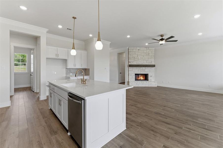 Open-concept living space featuring wood-finish flooring, a stone fireplace with wood mantel, and a ceiling fan