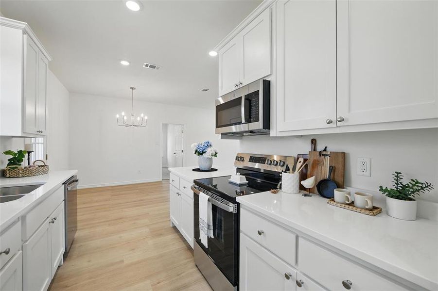 Kitchen with stainless steel appliances, a chandelier, light wood-style flooring, light countertops, and white cabinetry Kitchen with stainless steel appliances, a chandelier, light wood-style flooring, light countertops, and white cabinetry