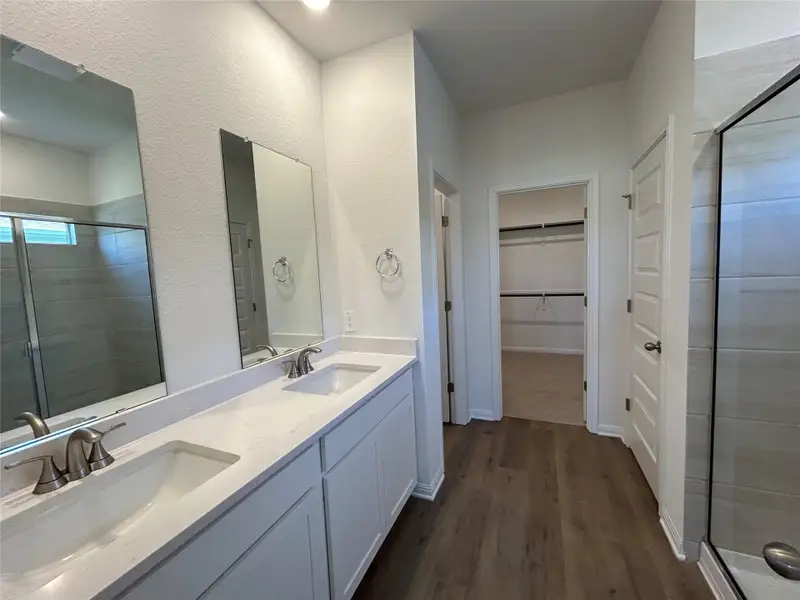 Bathroom with a shower stall, double vanity, dark wood finished floors, a spacious closet, and a textured wall Bathroom with a shower stall, double vanity, dark wood finished floors, a spacious closet, and a textured wall