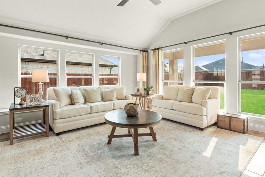 Bright living room with vaulted ceiling, two cream sofas, round wood coffee table, and large windows overlooking backyard