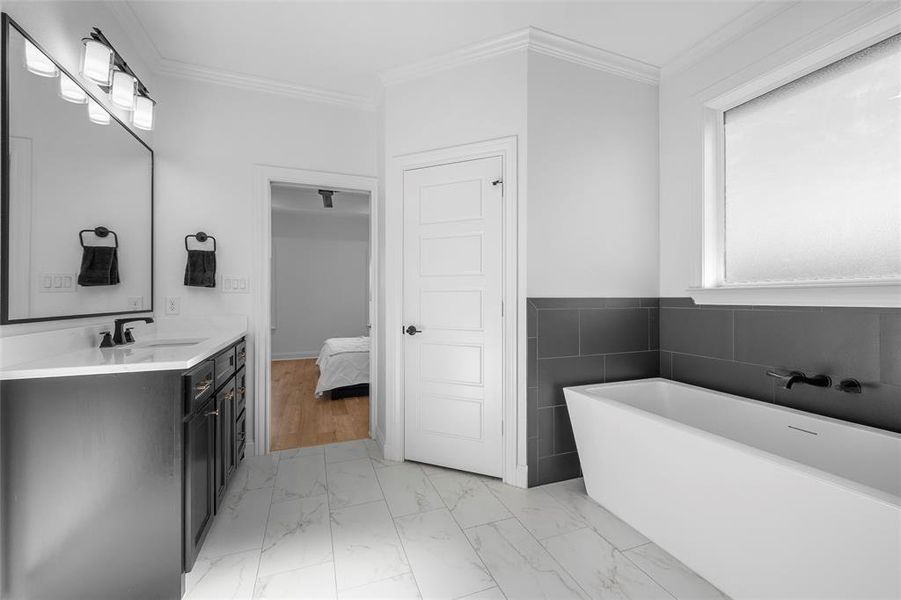 Bathroom with vanity, crown molding, a soaking tub, light marble finish floors, and ensuite bathroom Bathroom with vanity, crown molding, a soaking tub, light marble finish floors, and ensuite bathroom