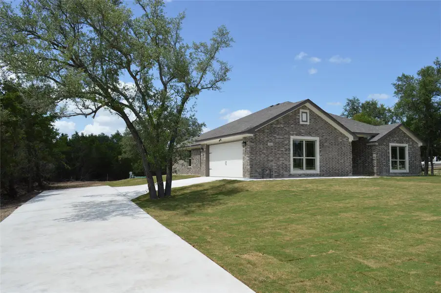 View of front of property featuring driveway, brick siding, a front lawn, and a garage