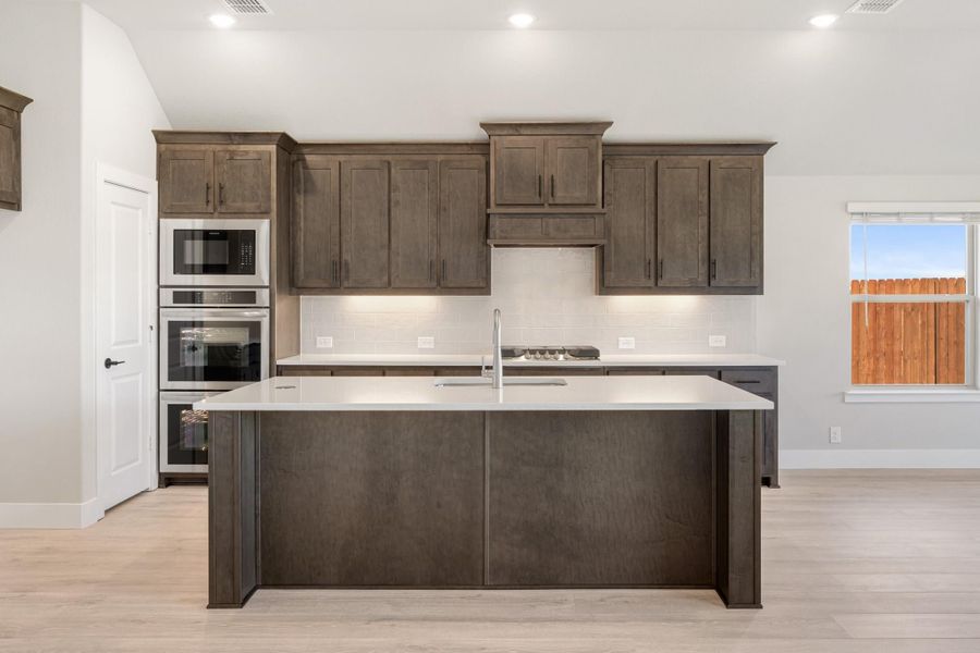 Kitchen with dark wood cabinets, large island with white countertop, and stainless steel double oven Kitchen with dark wood cabinets, large island with white countertop, and stainless steel double oven
