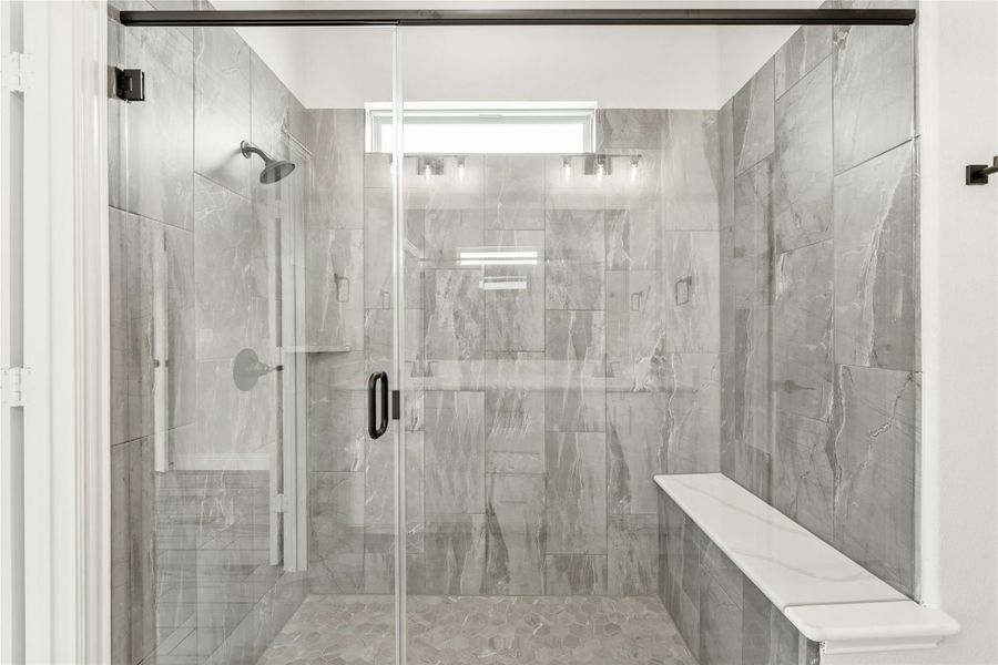 Walk-in shower with gray marble tile walls, glass door, built-in bench, and overhead window