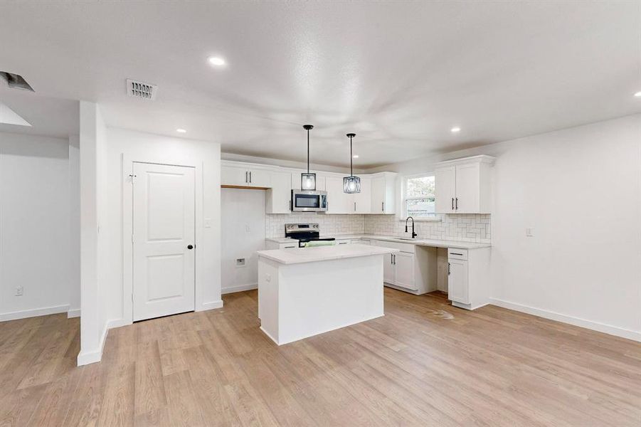 Kitchen featuring white cabinetry, stainless steel appliances, pendant lighting, a kitchen island, and light wood-type flooring