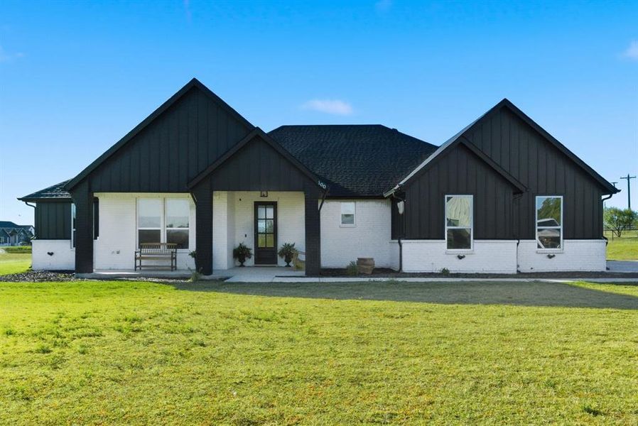 Modern farmhouse featuring board and batten siding, a front lawn, a porch, and brick siding