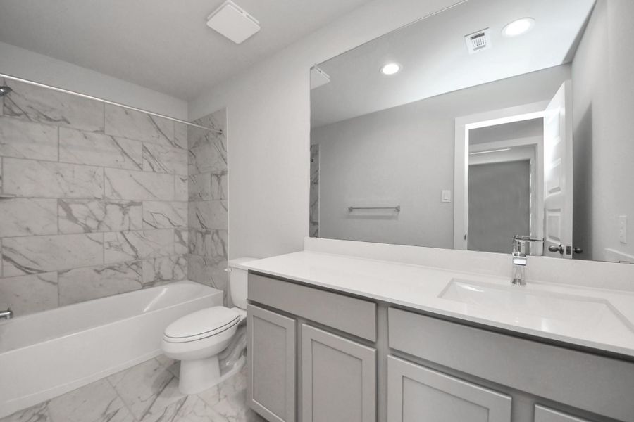 Secondary bath features tile flooring, bath/shower combo with tile surround, light stained wood cabinets, beautiful light countertop. Sample photo of completed home with similar floor plan. Actual colors and selections may vary.