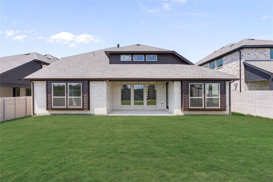 Rear exterior of single-story brick home with covered patio, large windows, and fenced backyard with green lawn.