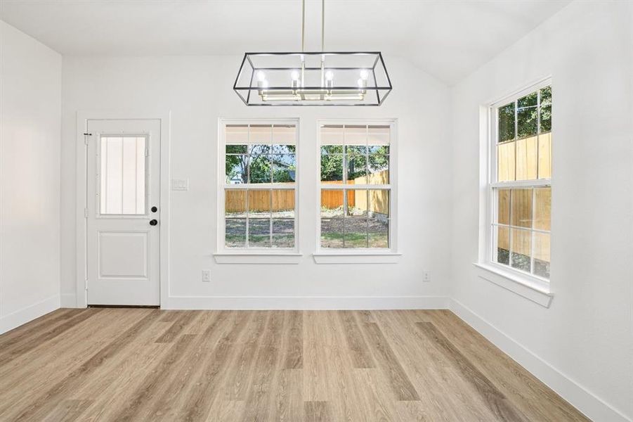Unfurnished dining area featuring light wood finished floors, lofted ceiling, and a chandelier Unfurnished dining area featuring light wood finished floors, lofted ceiling, and a chandelier