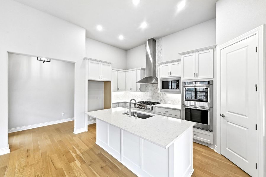 Contemporary kitchen featuring a large central island with sink, stainless steel appliances, white cabinetry, and wood-finish flooring