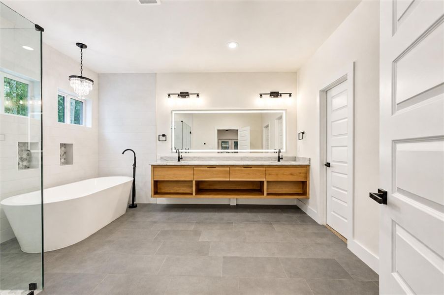 Luxurious Primary bathroom featuring a spacious freestanding tub, elegant chandelier, and a sleek double vanity all complemented by modern tile flooring.
