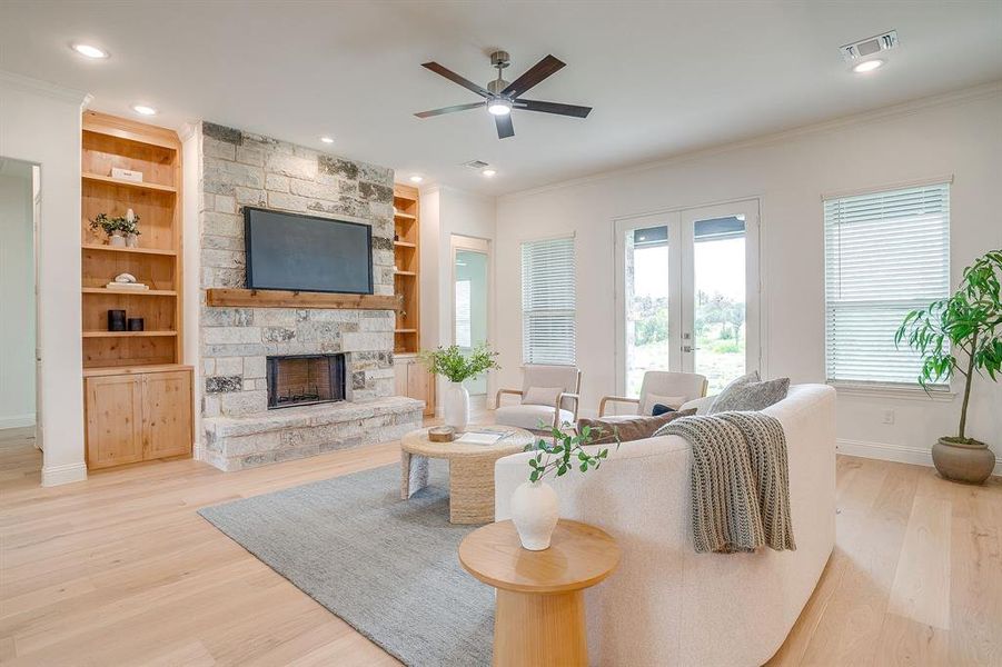Living area with built in adjustable shelves, light engineered wood flooring, a stone fireplace with solid cedar mantle, ceiling fan, and french doors that open to a covered back patio.