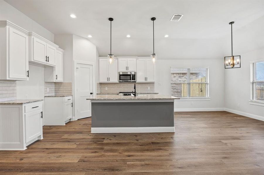 Kitchen with white cabinets, vaulted ceiling, light stone countertops, decorative light fixtures, and a center island with sink