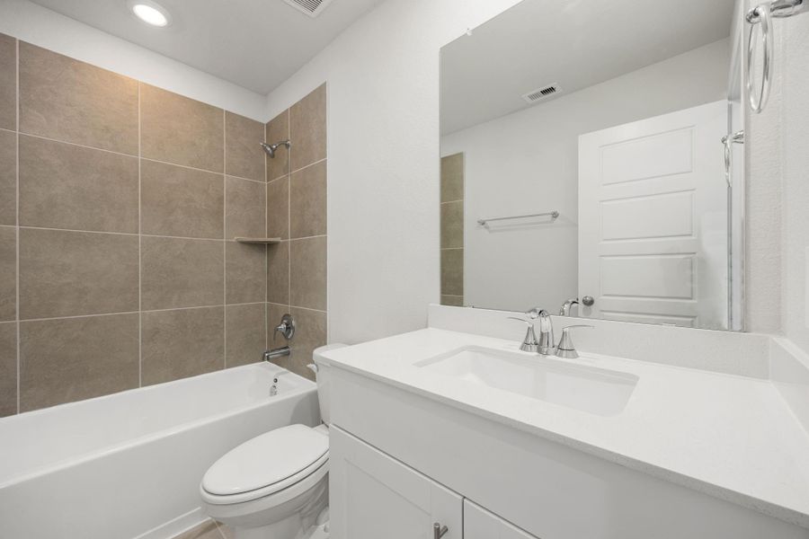 This full bathroom features sleek neutral tile, a modern vanity with quartz countertop, and a combination tub and shower, blending clean design with everyday functionality.