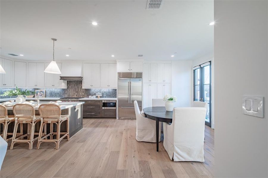 Kitchen featuring appliances with stainless steel finishes, light hardwood / wood-style floors, pendant lighting, white cabinets, and a kitchen island with sink