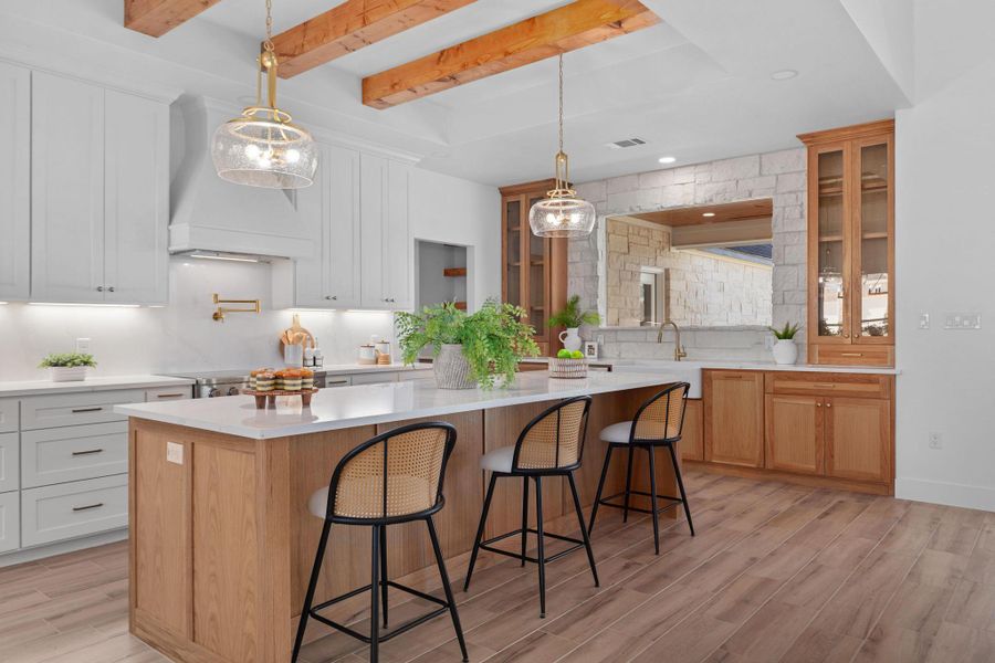 Two tone kitchen featuring a kitchen breakfast bar, light wood-style flooring, a kitchen island, glass fronted cabinets, and light stone counters Two tone kitchen featuring a kitchen breakfast bar, light wood-style flooring, a kitchen island, glass fronted cabinets, and light stone counters