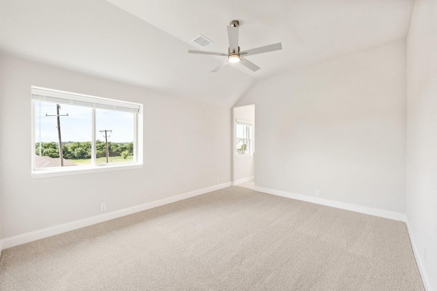 Empty bedroom with vaulted ceiling, ceiling fan, carpet flooring, and large window with outdoor view