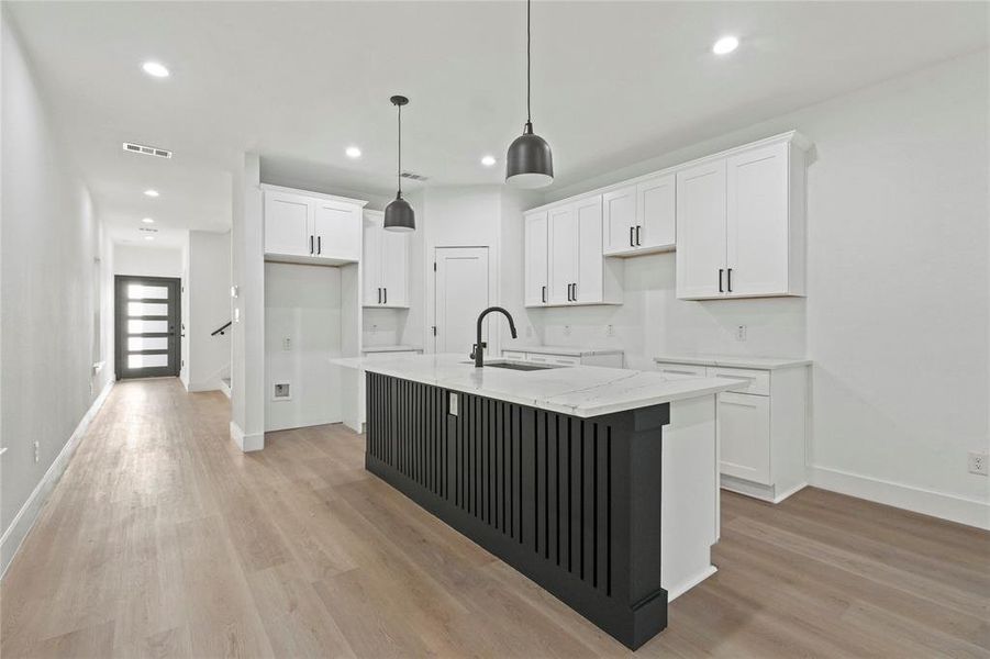 Kitchen with white cabinets, a center island with sink, light wood-type flooring, light stone countertops, and recessed lighting Kitchen with white cabinets, a center island with sink, light wood-type flooring, light stone countertops, and recessed lighting
