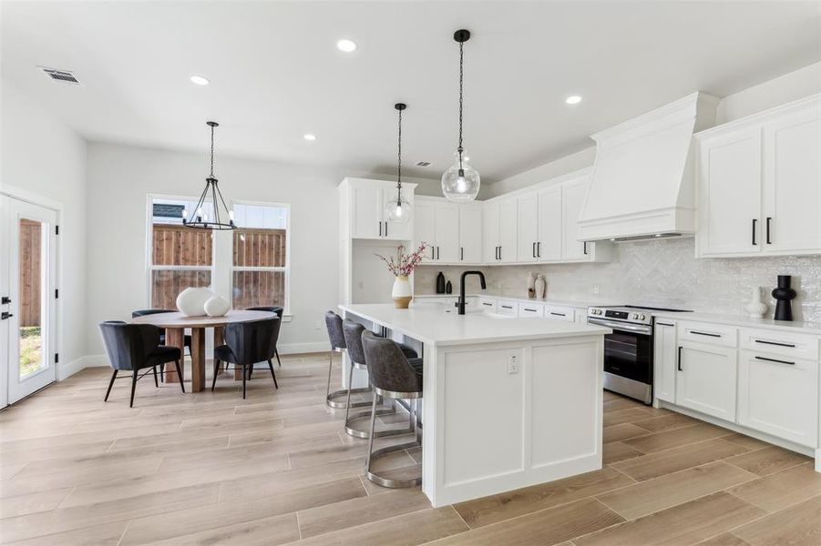 Kitchen with stainless steel electric stove, hanging light fixtures, tasteful backsplash, an island with sink, and custom exhaust hood