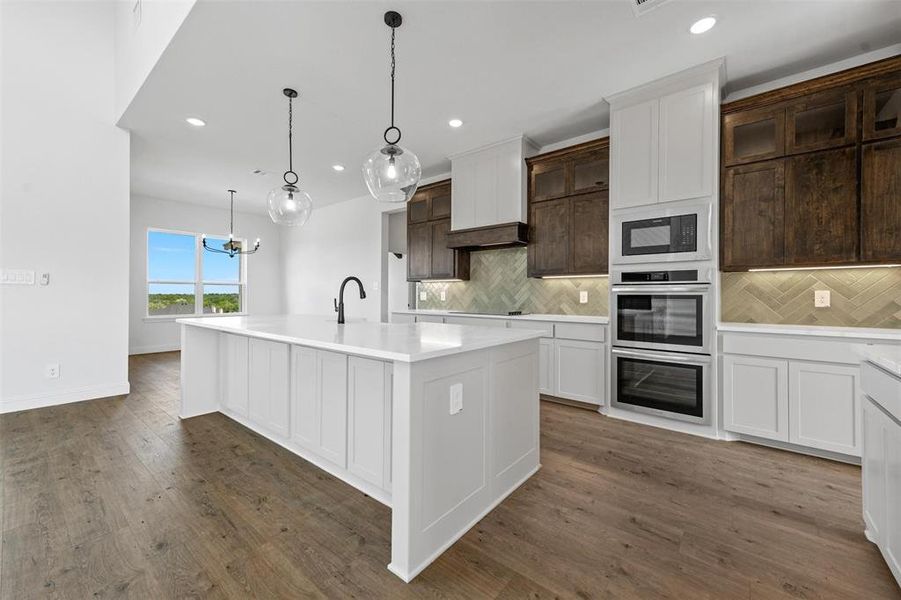 Kitchen featuring black appliances, a kitchen island with sink, dark hardwood / wood-style floors, decorative light fixtures, and backsplash