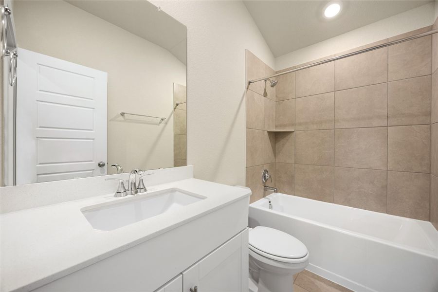 This full bathroom features sleek neutral tile, a modern vanity with quartz countertop, and a combination tub and shower, blending clean design with everyday functionality.