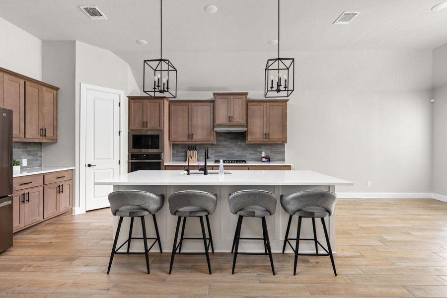 Two tone kitchen with a kitchen breakfast bar, hanging lights, light wood finished floors, a kitchen island with sink, and dual tone cabinets