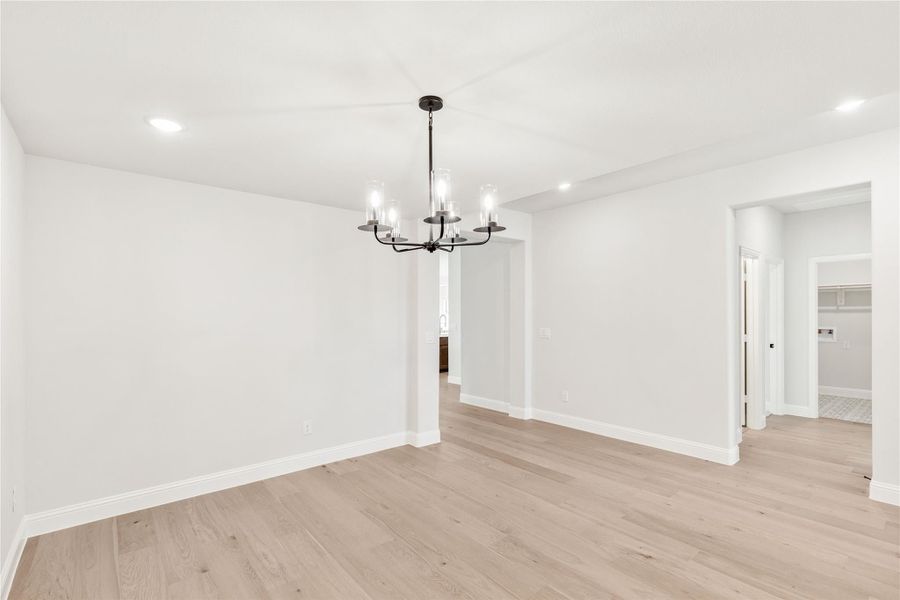 Empty dining room with black chandelier, light hardwood floors, and white walls