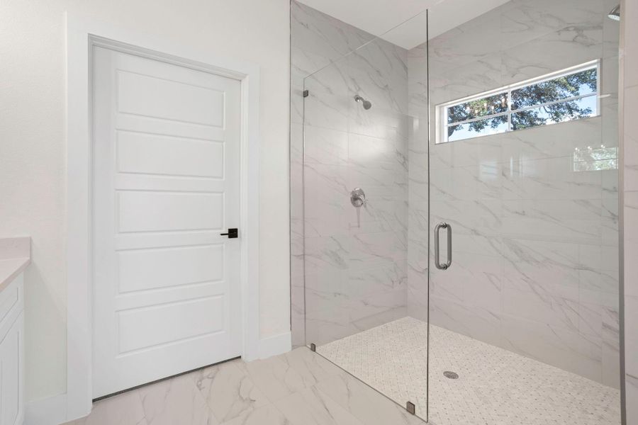 Spacious walk-in shower with clear glass enclosure, white marble-look wall tiling, and hexagon mosaic floor tiling Spacious walk-in shower with clear glass enclosure, white marble-look wall tiling, and hexagon mosaic floor tiling