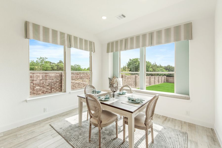 Bright dining nook with four-chair table, large windows, and backyard view on light wood floors Bright dining nook with four-chair table, large windows, and backyard view on light wood floors