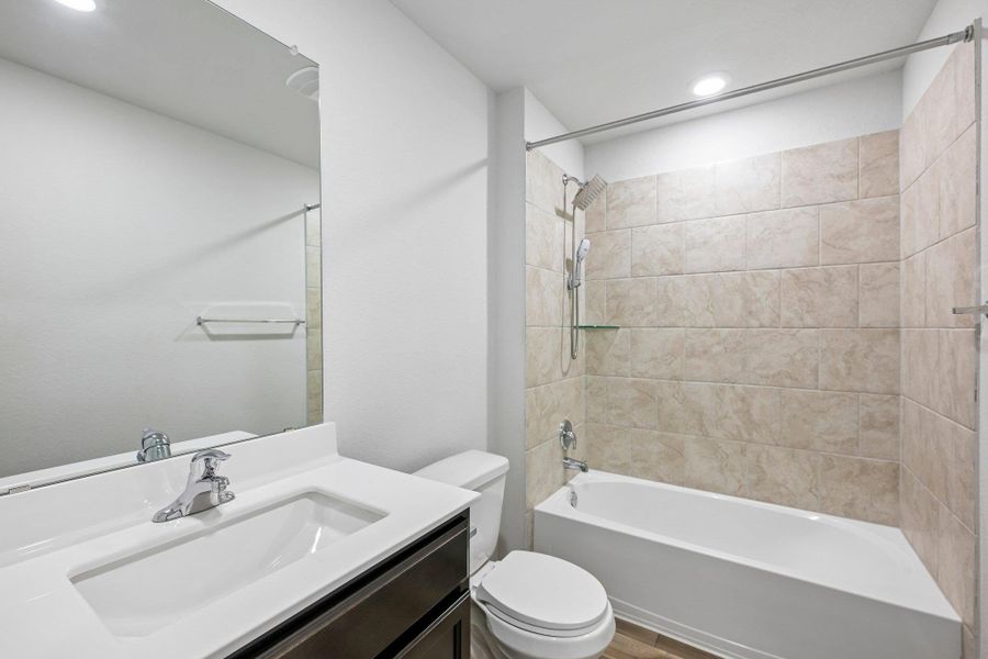 Bathroom featuring a vanity with an integrated sink and chrome fixtures, a full wall-mounted mirror, a toilet, a bathtub with a tiled surround, and a rain showerhead