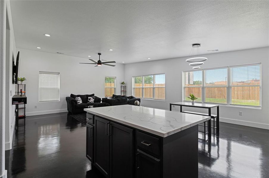 Kitchen with light stone counters, a kitchen island, a textured ceiling, hanging light fixtures, and ceiling fan