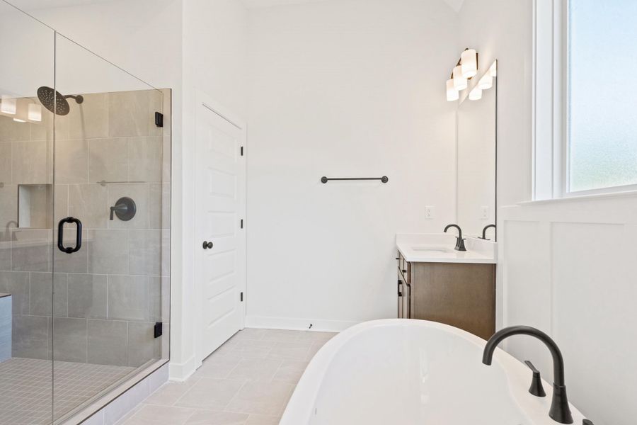 Freestanding soaking tub with matte black fixtures, glass-enclosed shower with tiled surround, single vanity with integrated sink, and paneling detail below the frosted window Freestanding soaking tub with matte black fixtures, glass-enclosed shower with tiled surround, single vanity with integrated sink, and paneling detail below the frosted window