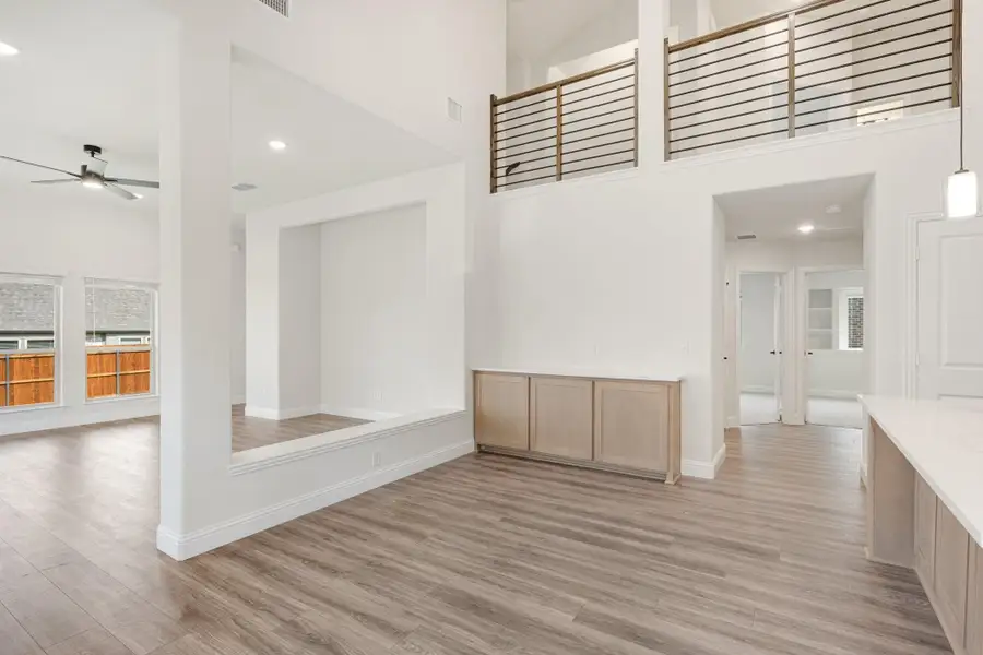 Open-concept living area with two-story ceiling, wood floors, and upper-level metal railing balcony