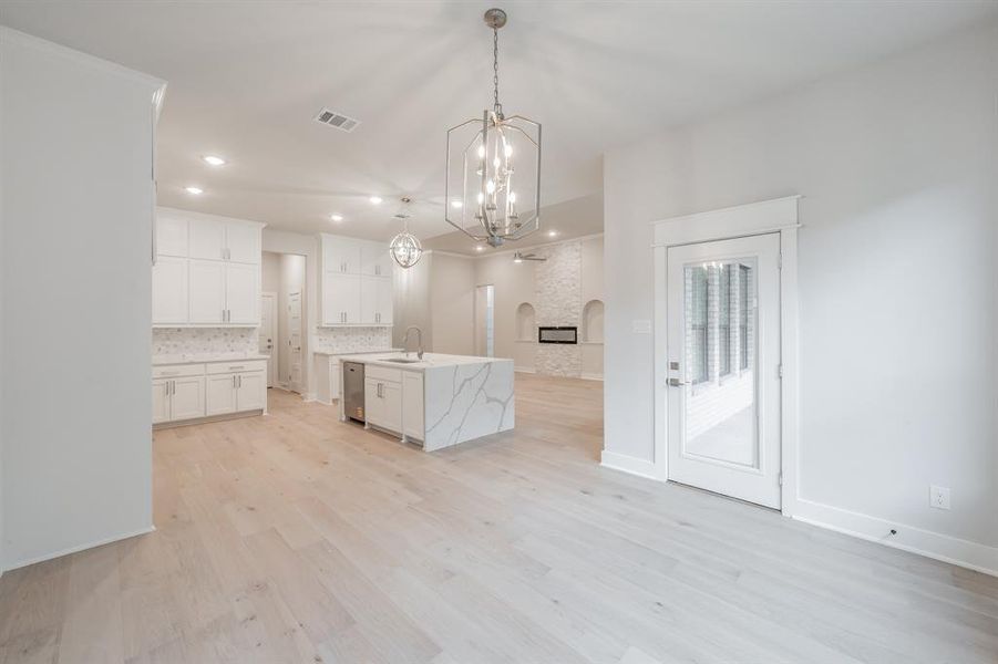 Kitchen with white cabinetry, hanging light fixtures, a center island with sink, light stone counters, and light wood-style flooring