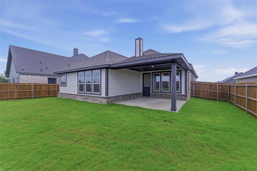 Expansive green lawn with a covered patio, featuring a dark gray roofline, white siding, and a stone-clad foundation