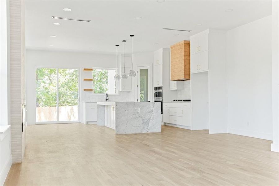 Kitchen with a center island, hanging light fixtures, light hardwood / wood-style flooring, white cabinets, and backsplash