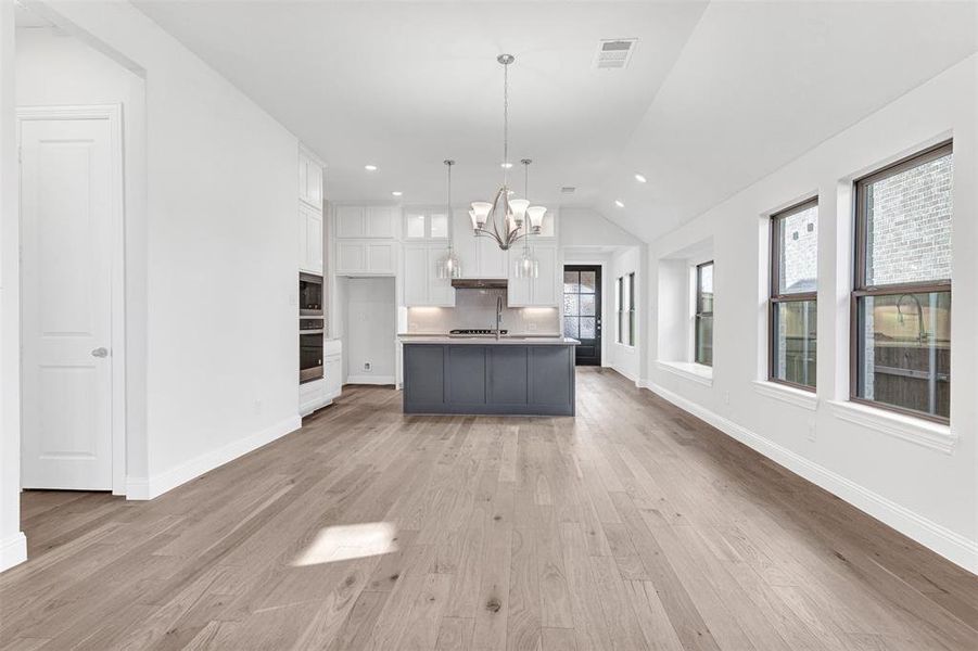 Kitchen with white cabinetry, an island with sink, oven, decorative light fixtures, and light wood-type flooring