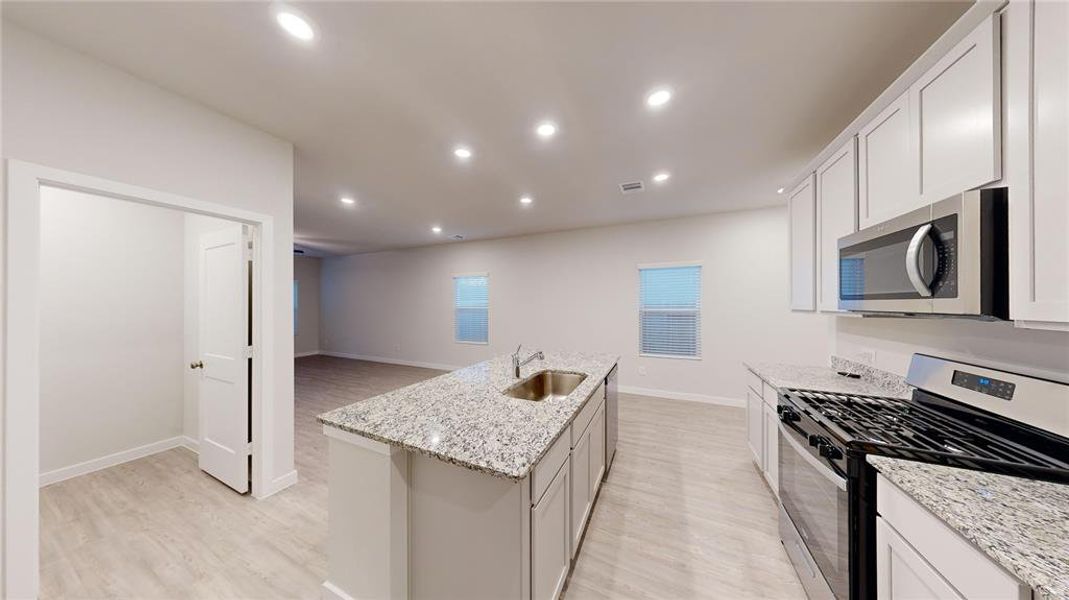 Modern kitchen with granite countertops, stainless steel appliances, and ample cabinetry. An open layout with recessed lighting and light wood color flooring enhances spaciousness.