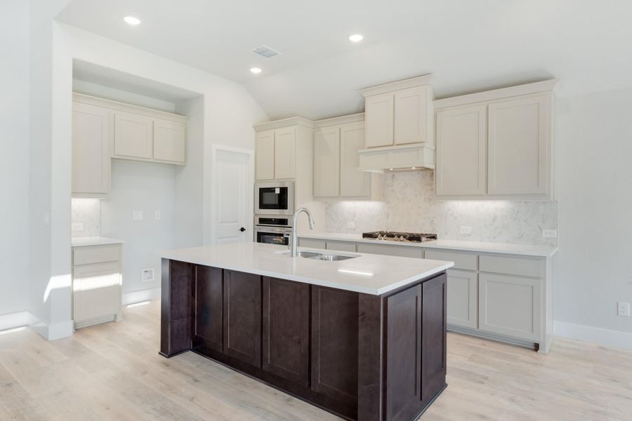 Kitchen with dark wood island, white countertops, cream cabinets, marble backsplash, and stainless steel appliances