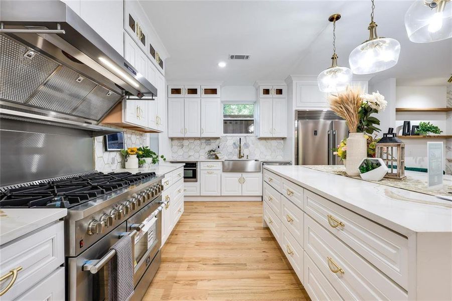 Kitchen with pendant lighting, sink, white cabinetry, high end appliances, and extractor fan