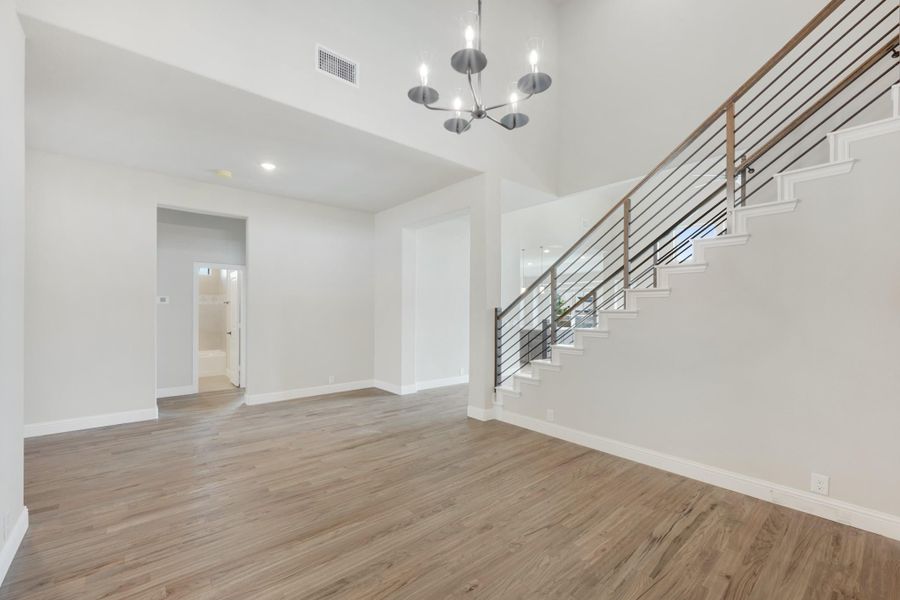 Open living area with hardwood floors, modern chandelier, and staircase with metal railing Open living area with hardwood floors, modern chandelier, and staircase with metal railing