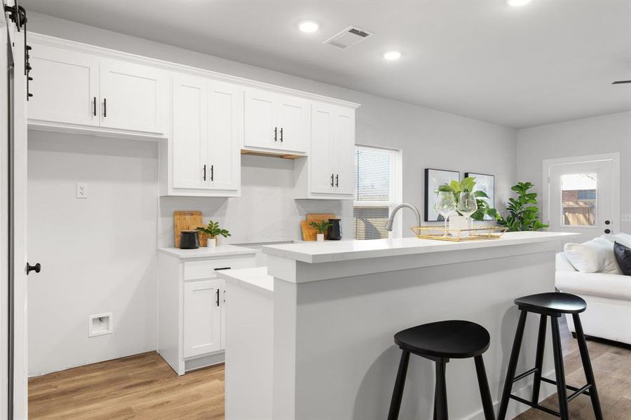 Kitchen with white cabinetry, light wood-style flooring, visible vents, and a wealth of natural light