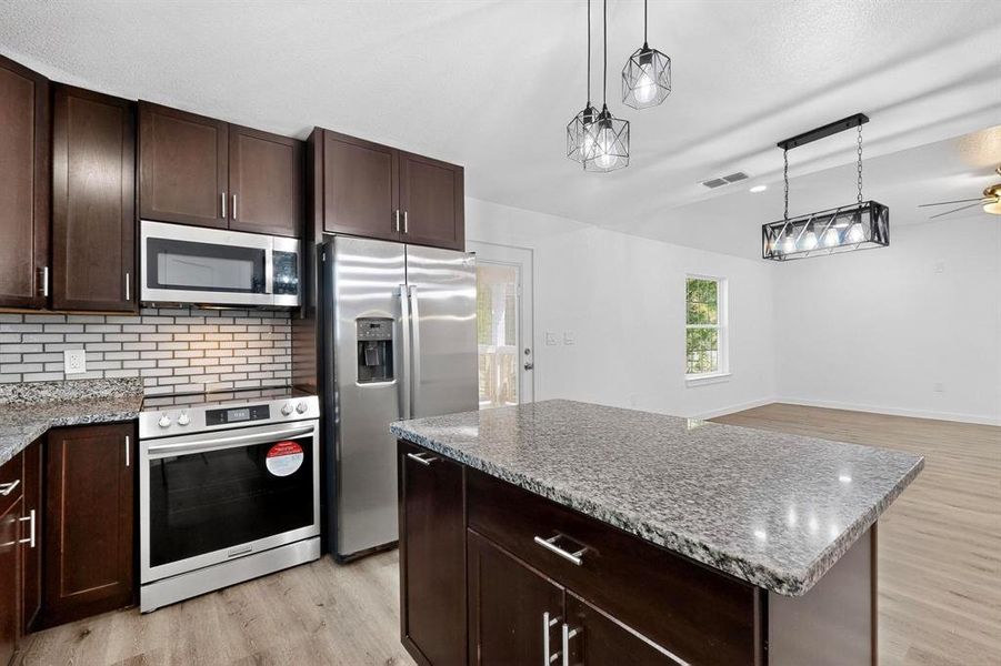 Kitchen with dark brown cabinetry, stainless steel appliances, light wood-type flooring, and tasteful backsplash