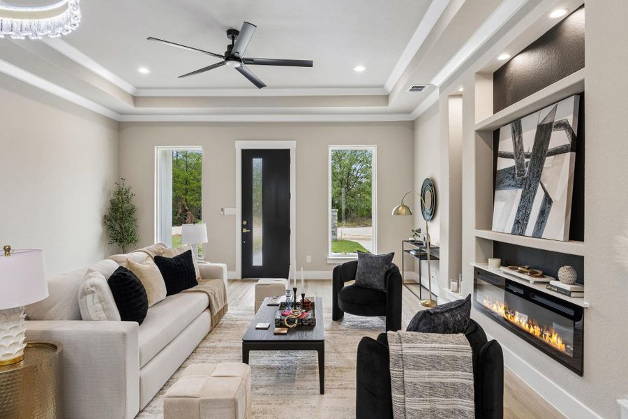 Recessed lighting illuminates this bright living room, featuring a sleek fireplace and elegant tray ceilings.