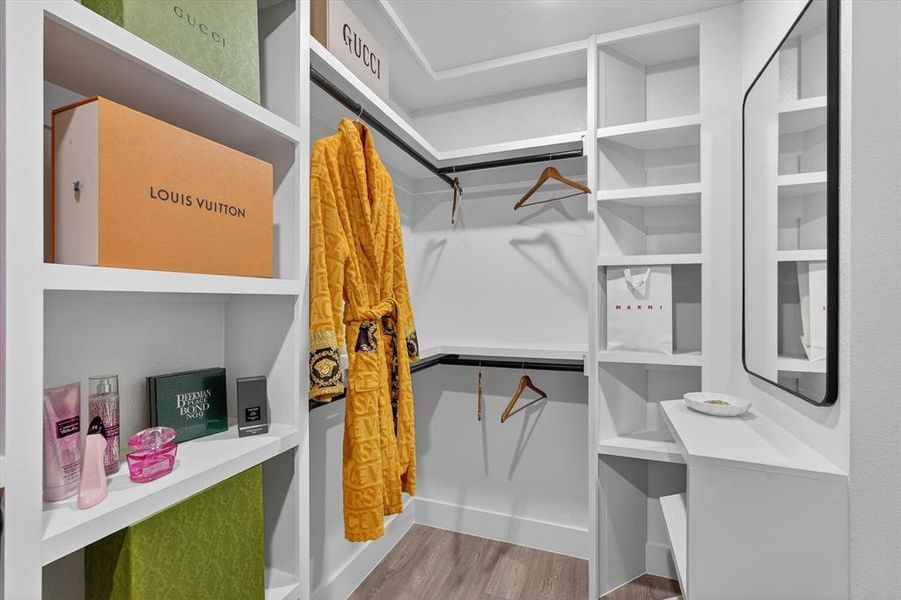 Custom closet featuring extensive built-in shelving, hanging rods, wood-finish flooring, and a wall-mounted mirror