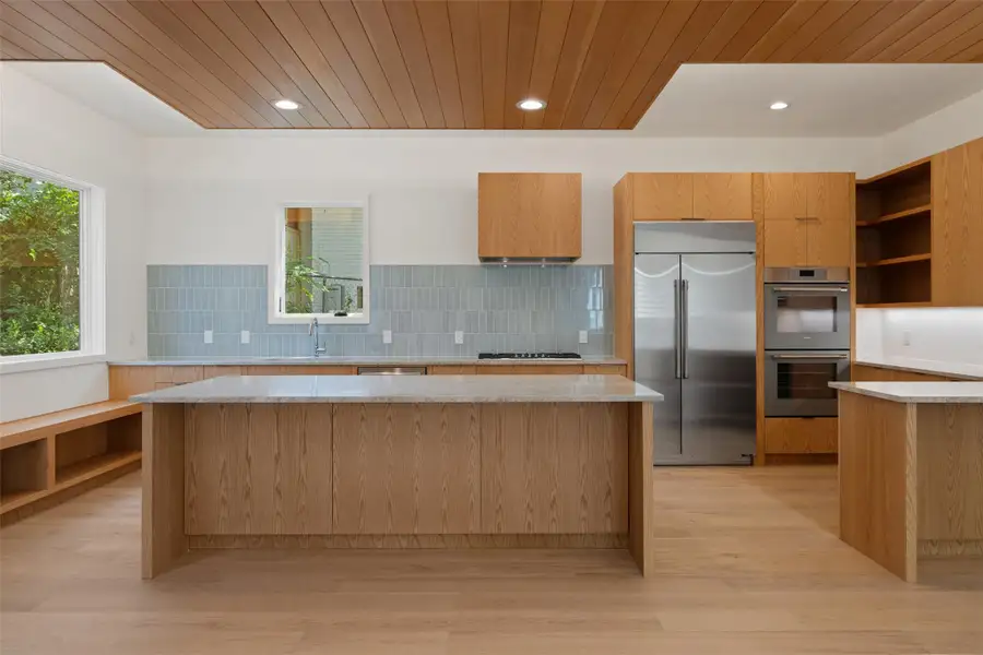 Kitchen with stainless steel appliances, open shelves, modern cabinets, light stone countertops, and wooden ceiling Kitchen with stainless steel appliances, open shelves, modern cabinets, light stone countertops, and wooden ceiling