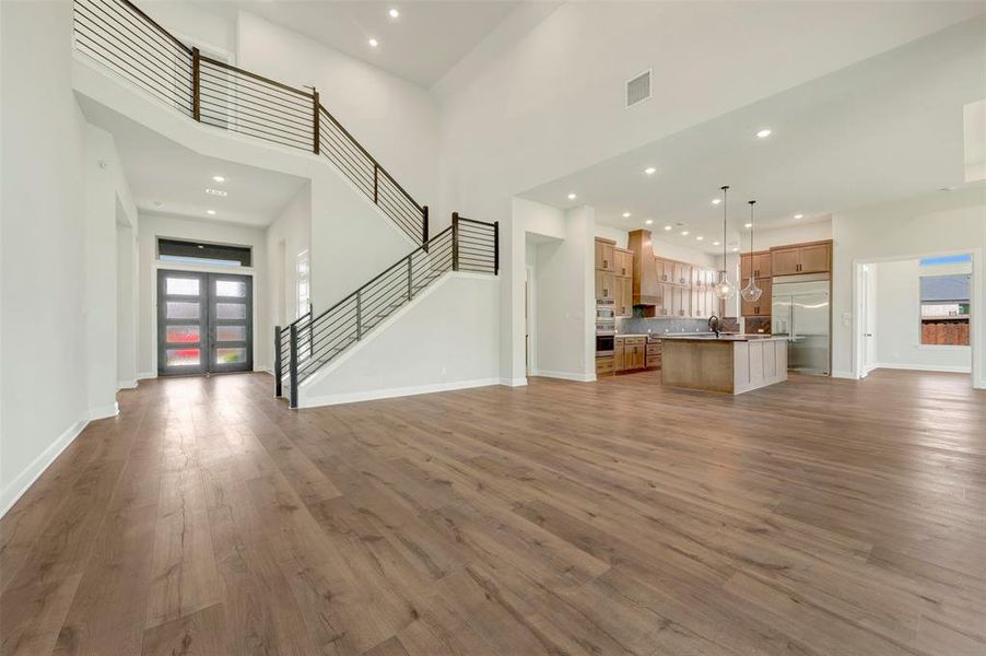 Unfurnished living room featuring a high ceiling, light wood-type flooring, french doors, and recessed lighting