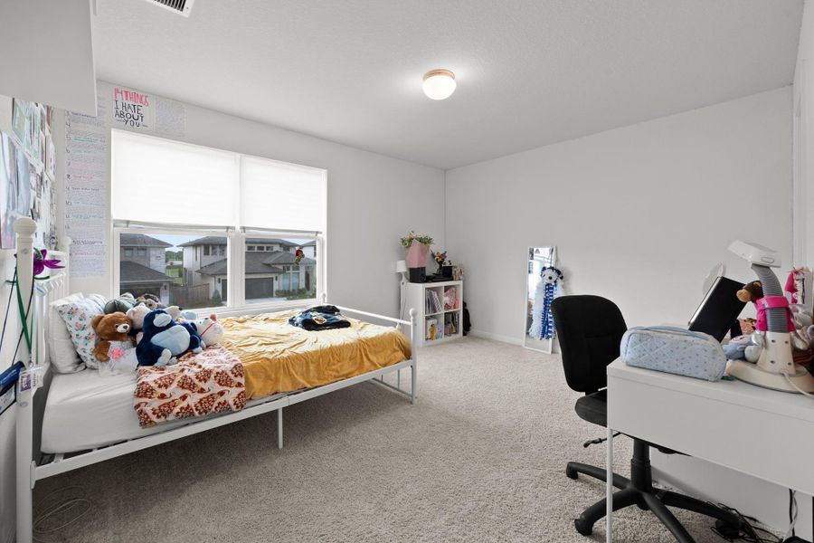 Carpeted room featuring a large window with white blinds, a white built-in desk, and a ceiling-mounted light fixture